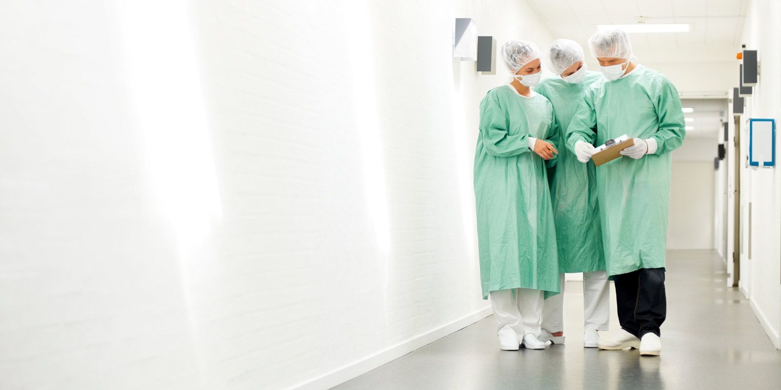 Three people of different genders in surgical clothing are standing in a hospital corridor discussing something