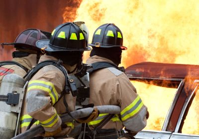 Drei Feuerwehrmänner von hinten beim Löschen eines Fahrzeugbrands