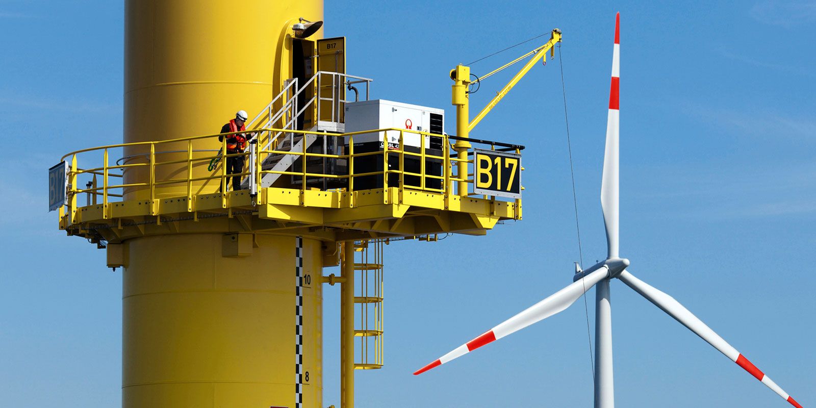 Service technician stands on a platform on the mast of a wind turbine